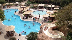 Un área de piscina con varias piscinas, sillas de descanso, sombrillas y una formación rocosa.
