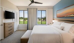 A hotel room with a large bed, a flat-screen TV mounted on the wall, a ceiling fan, and a large window with a view of a golf course.