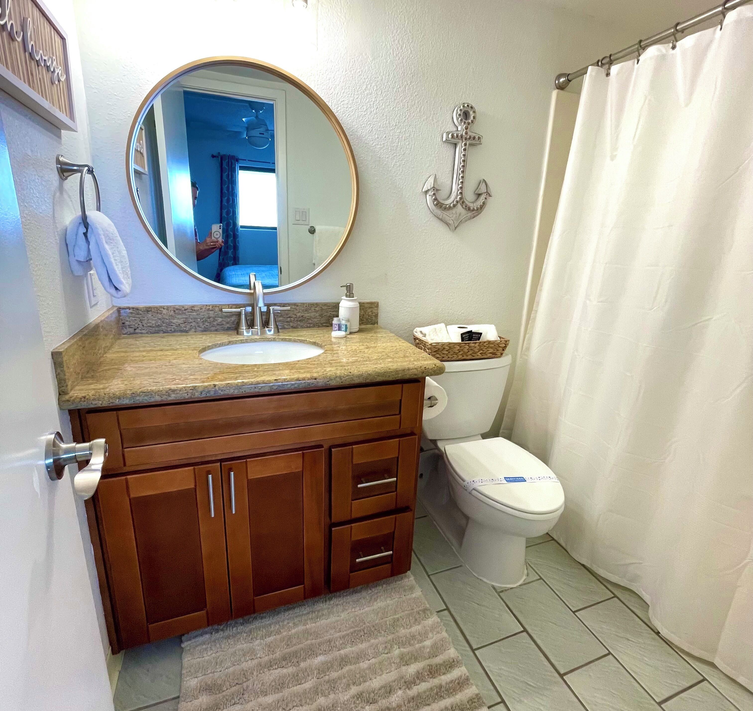 A bathroom with a wooden vanity, a round mirror, a toilet, and a shower curtain.