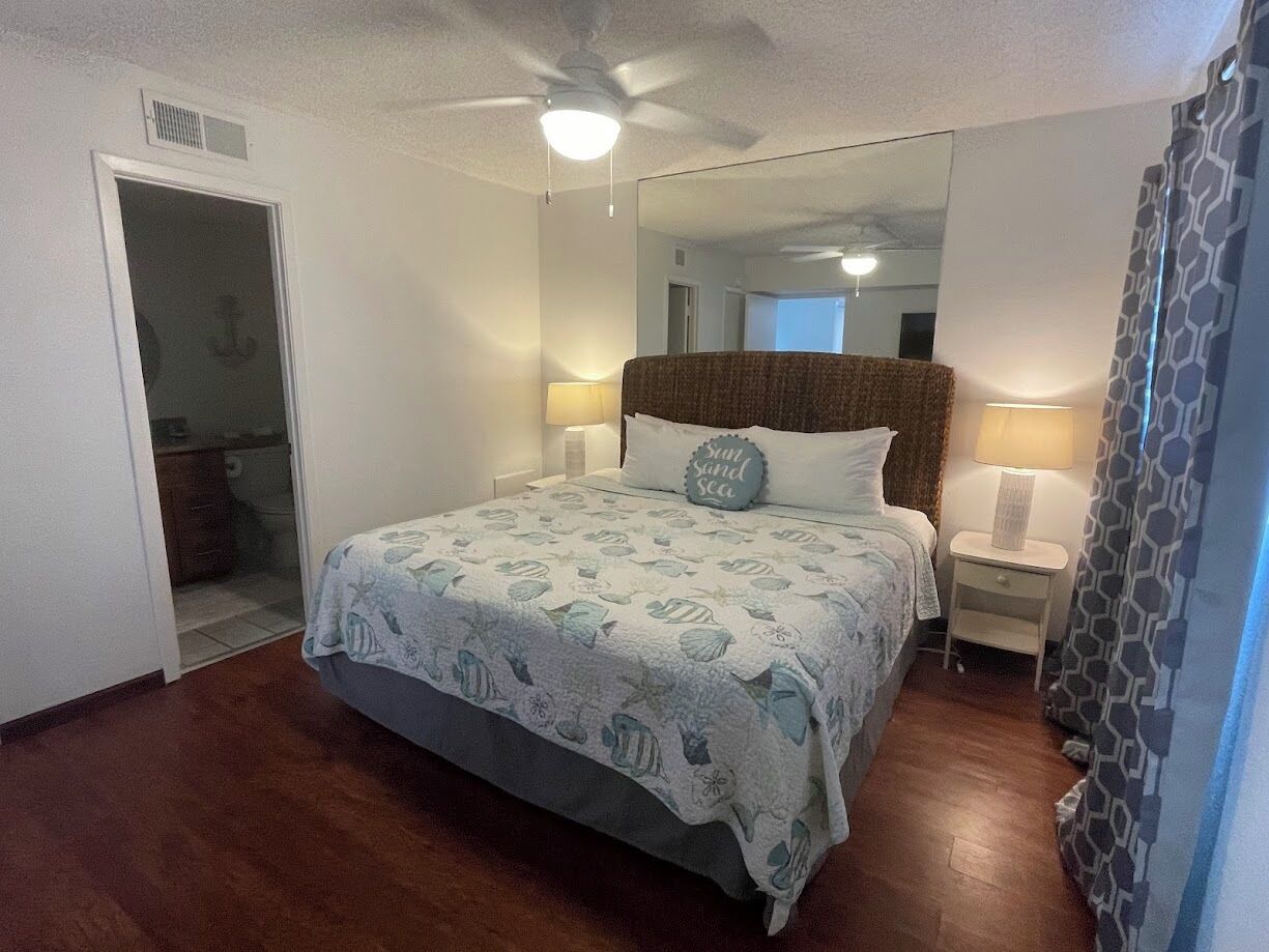 A bedroom with a bed, two bedside tables, a ceiling fan, and a door leading to a bathroom.