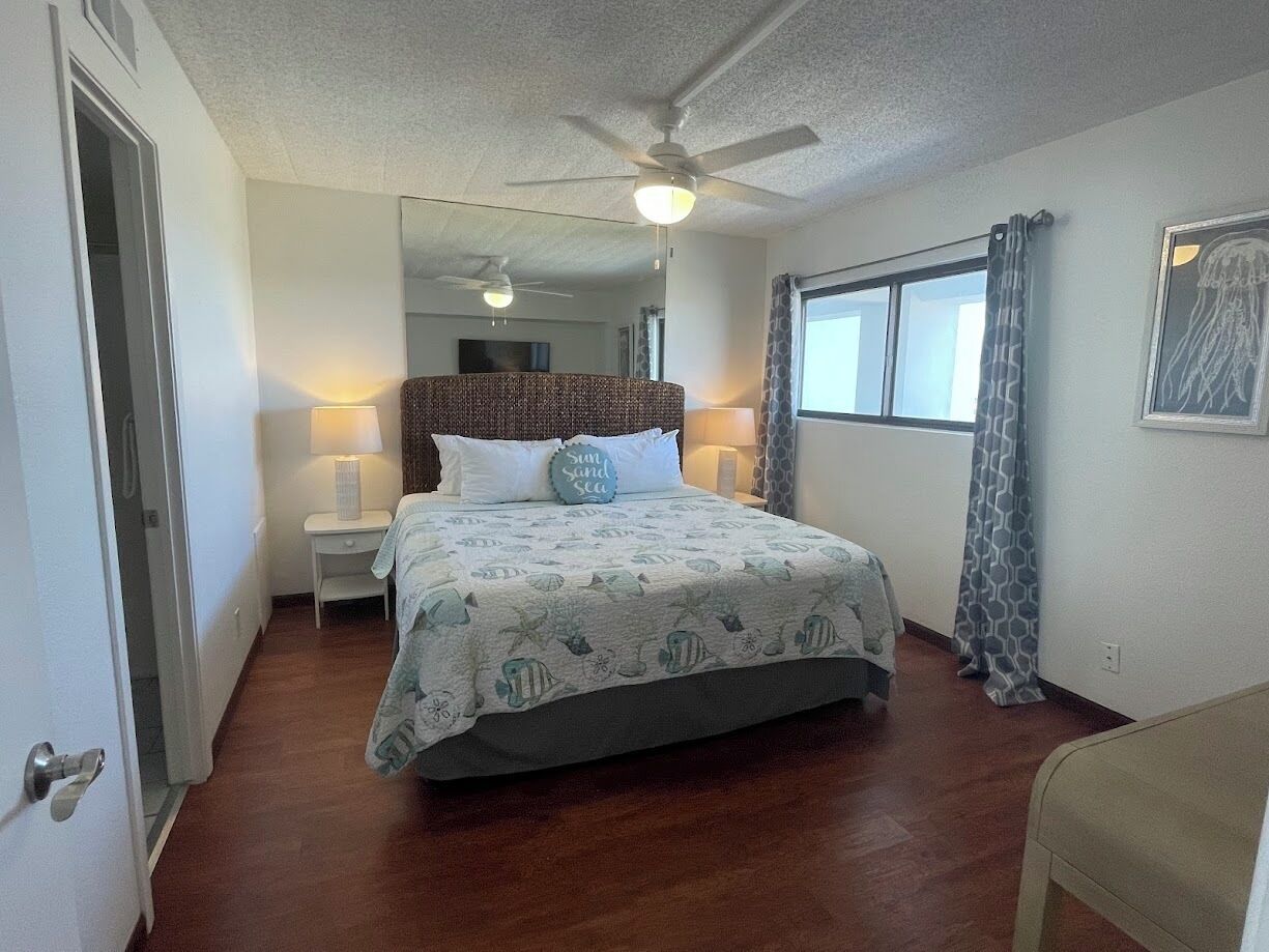 A bedroom with a bed, a ceiling fan, a window with curtains, and a door.