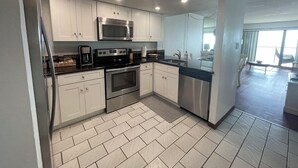 Cozinha moderna com armários brancos, eletrodomésticos de aço inoxidável e piso de azulejos em padrão herringbone.