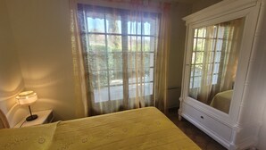 Un dormitorio con cama, mesita de noche, lámpara, armario y ventana con cortinas.