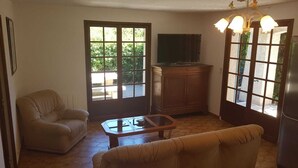 Una sala de estar con sofá, una mesa de centro de vidrio, un televisor sobre un mueble bajo y un aparador.