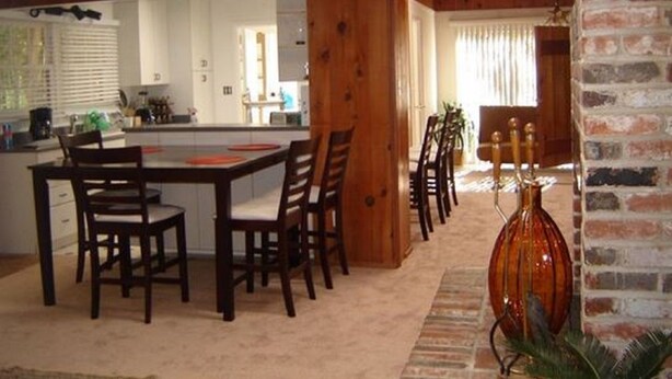 Een eethoek met een houten tafel en stoelen, een bakstenen open haard en uitzicht op de keuken.