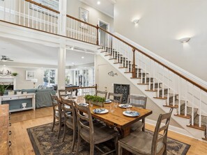 A spacious dining area with a wooden table set for six, surrounded by dark wooden chairs. A staircase with white railings and wooden steps leads to an upper level. - Lovely Two Story Home Near the Beach (Hilton Head Island)