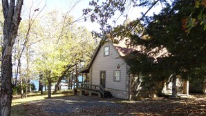 A small stone building with a porch, surrounded by trees and a pathway covered with fallen leaves.