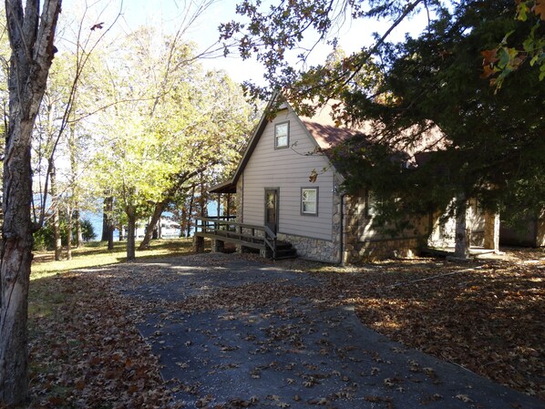 A small stone building with a porch, surrounded by trees and a pathway covered with fallen leaves.