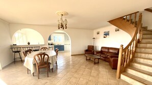A spacious living room with a dining area, a staircase, and a kitchen visible through an archway. - Farniente & sunsets on the Gulf of Ajaccio and the Sanguinaires Islands (Bastelicaccia)
