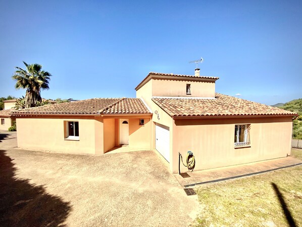 A two-story building with a tiled roof, a small balcony, and a hose attached to the exterior wall.