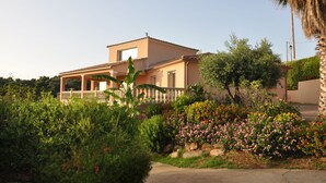 A two-story house with a balcony, surrounded by lush greenery and colorful flowers. - Farniente & sunsets on the Gulf of Ajaccio and the Sanguinaires Islands (Bastelicaccia)