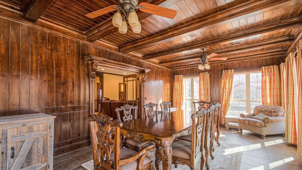 Ein Esszimmer mit Holzboden, einem großen Tisch und Stühlen, einem Deckenventilator und einem Fenster mit Vorhängen.