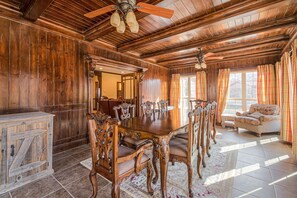 Een houten eetkamer met een grote tafel en stoelen, een plafondventilator en een raam met gordijnen.