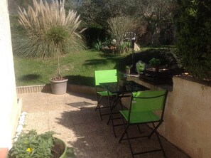 En terrasse med bord og stole, omgivet af plantekasser og en græsplæne.