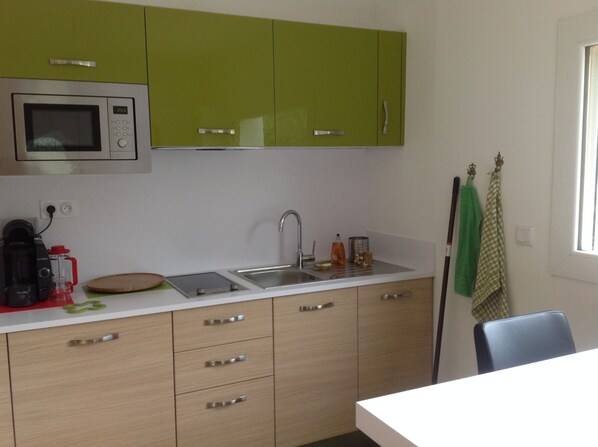 Een keuken met groene kastjes, een magnetron, een spoelbak en een raam.