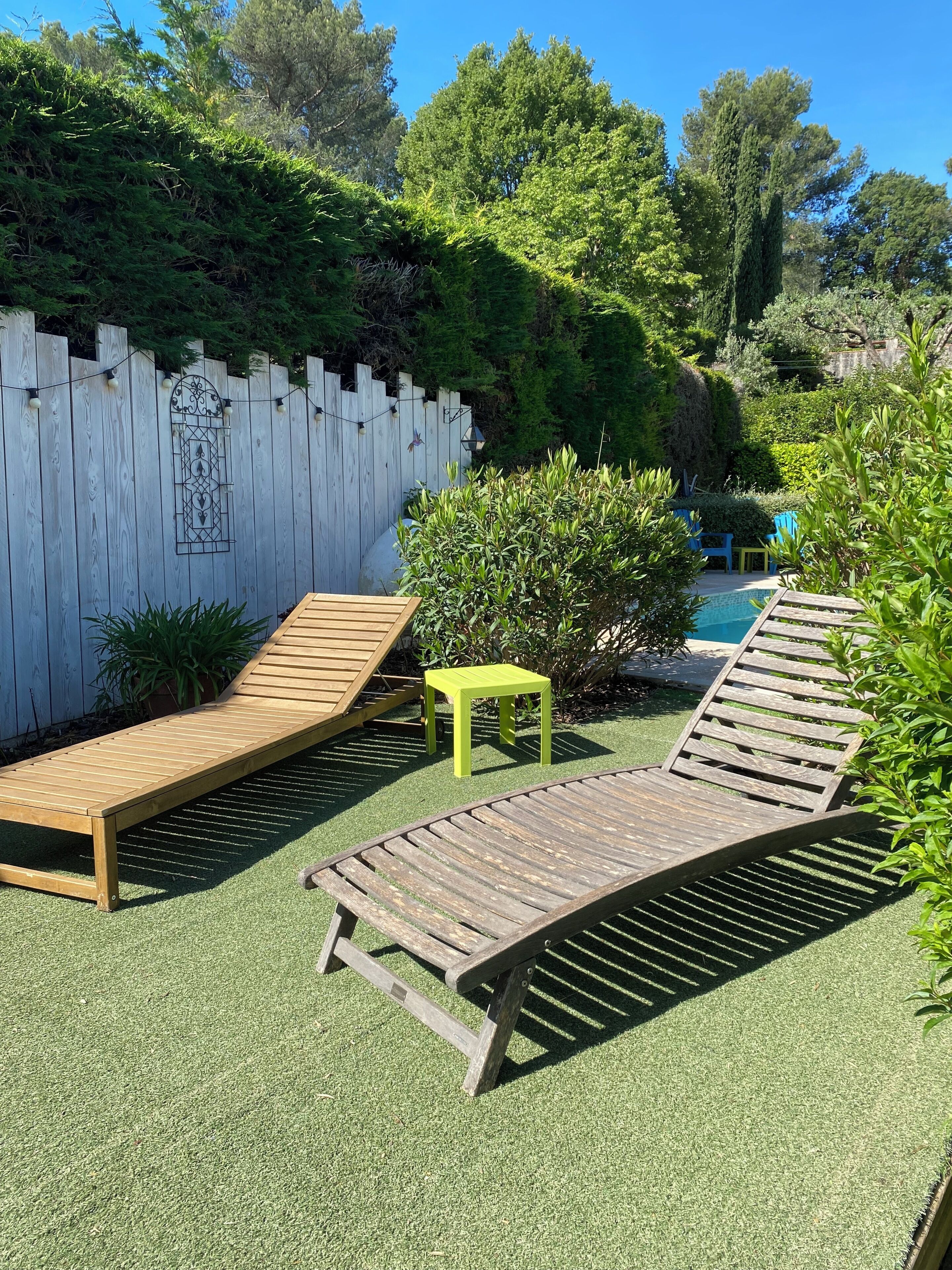 Ein Garten mit einer Holzterrasse, einem kleinen Pool und einem weißen Zaun.