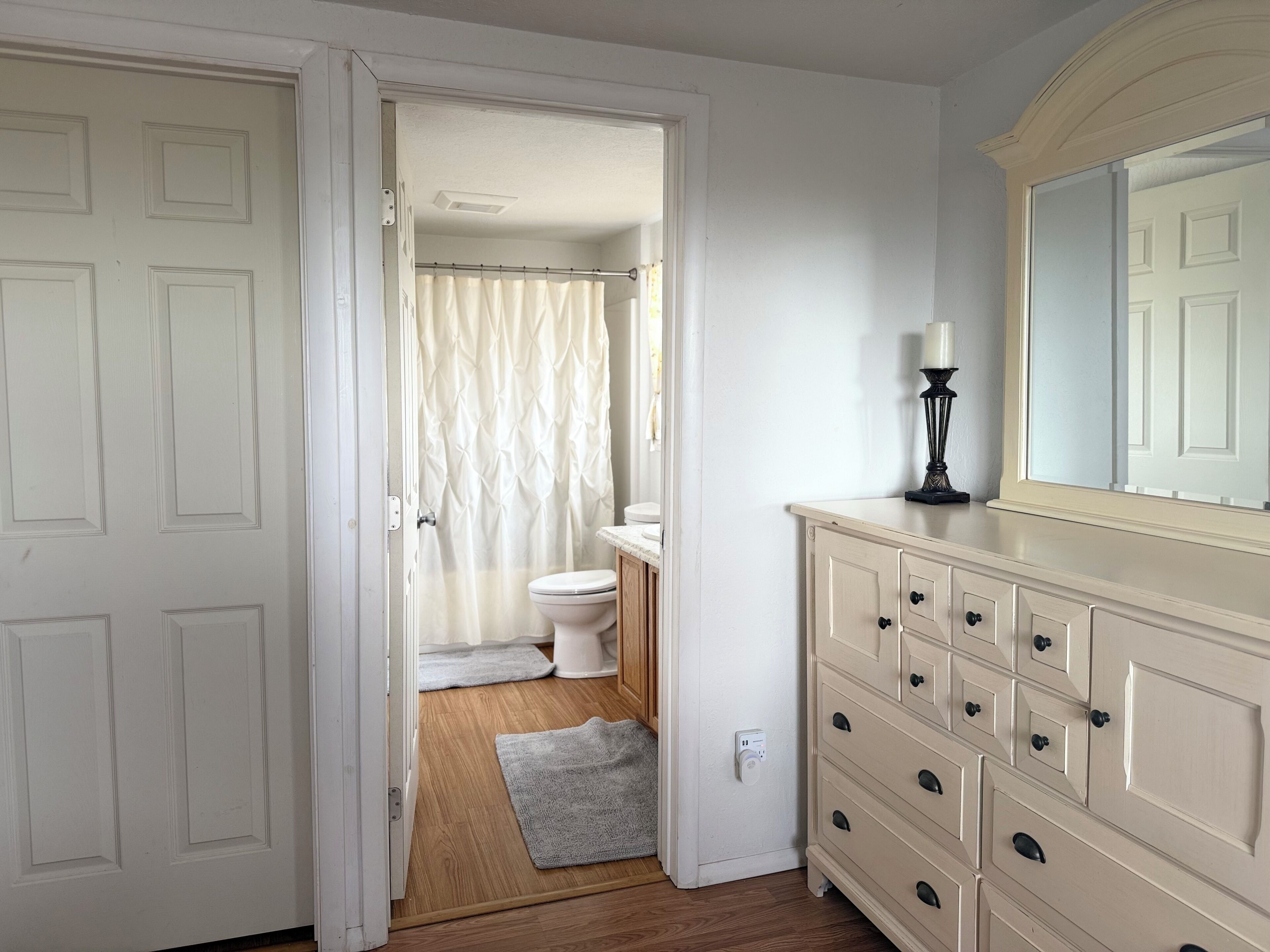 Een badkamer met toilet, douchegordijn en een wastafel met spiegel en lamp.