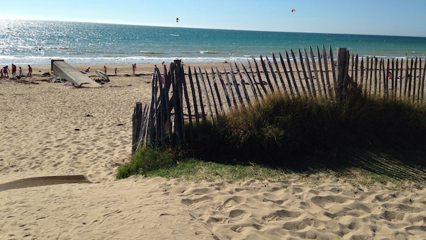 Una playa arenosa con una cerca de madera, una torre de salvavidas y el océano al fondo.