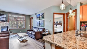 A modern living room with a fireplace, leather sofa, and a dining area with granite countertops. - Inviting Condo – Hot Tub & Relaxing Atmosphere! (Canmore)