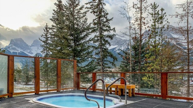 A hot tub with a mountain view, surrounded by wooden railings and a bench. - Inviting Condo – Hot Tub & Relaxing Atmosphere! (Canmore)