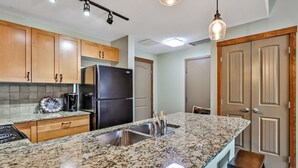 A kitchen with granite countertops, stainless steel appliances, wooden cabinets, and a hanging light fixture. - Inviting Condo – Hot Tub & Relaxing Atmosphere! (Canmore)