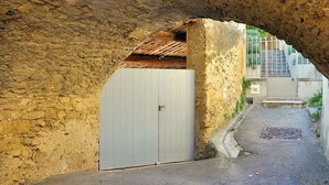 Uma passagem subterrânea com um portão branco, paredes de pedra e um caminho pavimentado.