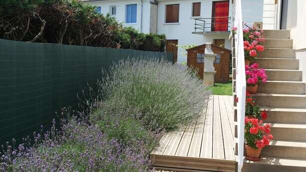 A wooden deck with a green fence, lavender plants, and a staircase leading to a house with a red door. - Apartment 1 * "The House of the Artist" (Coulounieix-Chamiers)