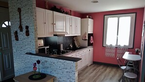 A kitchen with white cabinets, a black countertop, and a wooden floor. There is a window with curtains and a small dining area with a table and chairs. - Apartment 1 * "The House of the Artist" (Coulounieix-Chamiers)