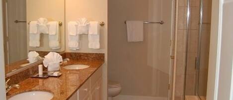 A bathroom with two sinks, a toilet, a shower, and a towel rack with multiple towels.