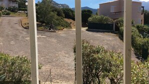 A parking area with a dirt path leading to a building, surrounded by greenery and mountains in the background. - The most beautiful place in corsica, beaches, garden, terrace, private parking (Lumio)