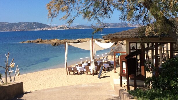 A beachside restaurant with outdoor seating, a thatched roof, and a view of the sea and distant hills. - The most beautiful place in corsica, beaches, garden, terrace, private parking (Lumio)