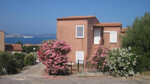A two-story building with a red-tiled roof, a staircase leading to the upper floor, and a view of the sea in the background. - The most beautiful place in corsica, beaches, garden, terrace, private parking (Lumio)