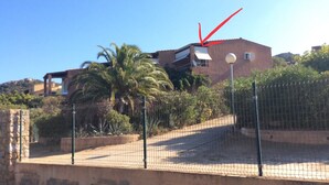 A fenced outdoor area with a building in the background, a palm tree, and a street lamp. - The most beautiful place in corsica, beaches, garden, terrace, private parking (Lumio)