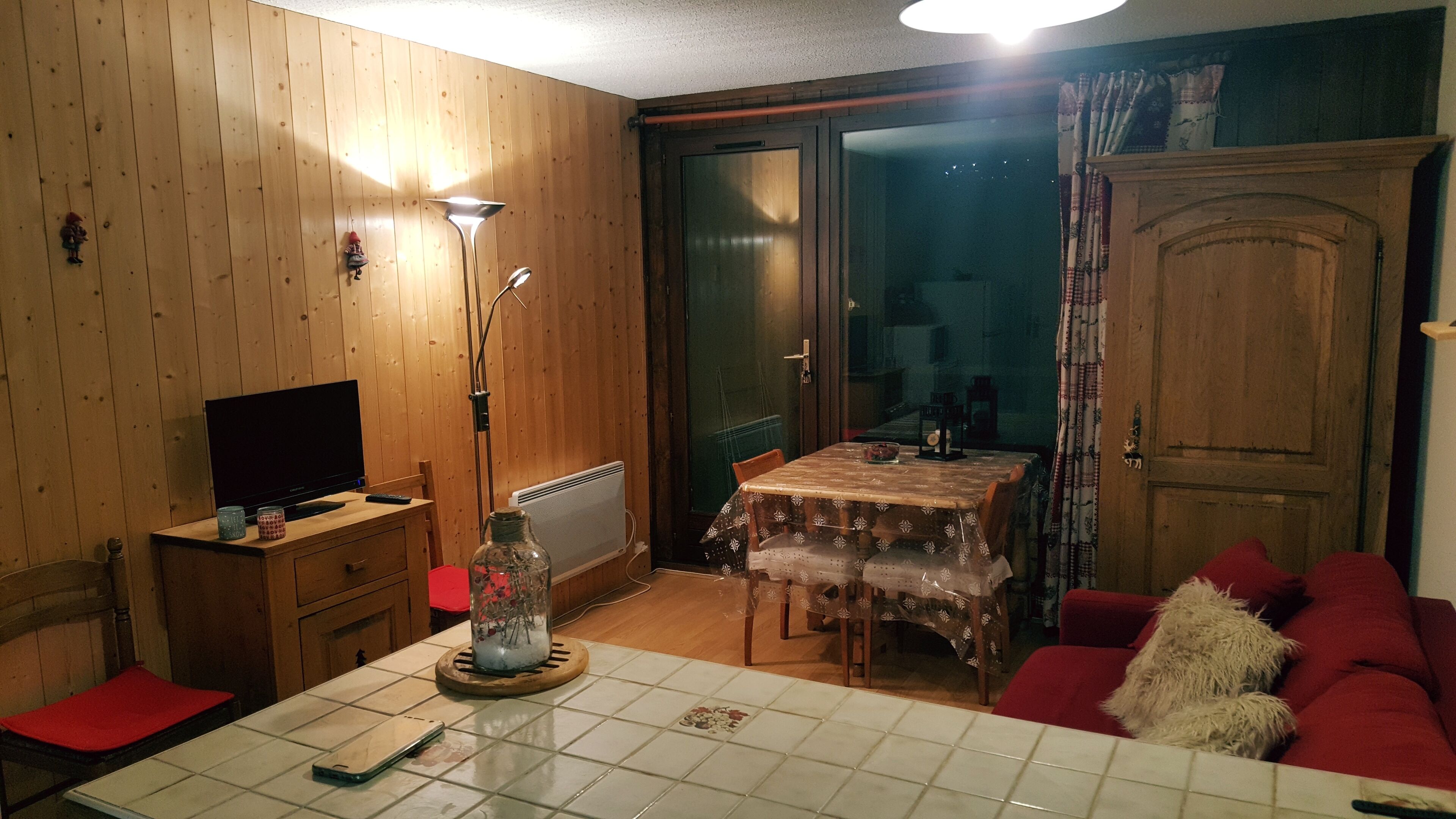Een gezellige woonkamer met houten wanden, een eettafel met een tafelkleed met patroon, een rode bank en een televisie op een houten kast.
