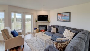 A modern living room with a grey sofa, a white coffee table, and a fireplace. There is a large window with a view of the outdoors. - Beach Please- Oceanfront easy access to the beach (Long Beach)