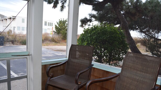 A covered porch with two wicker chairs and a view of a building and trees. - Pet Friendly Ocean Front Building Downtown Dewey Beach Sleeps 7 (Dewey Beach)