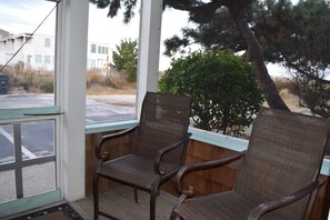 Une véranda couverte avec deux fauteuils en osier et une vue sur un bâtiment et des arbres.