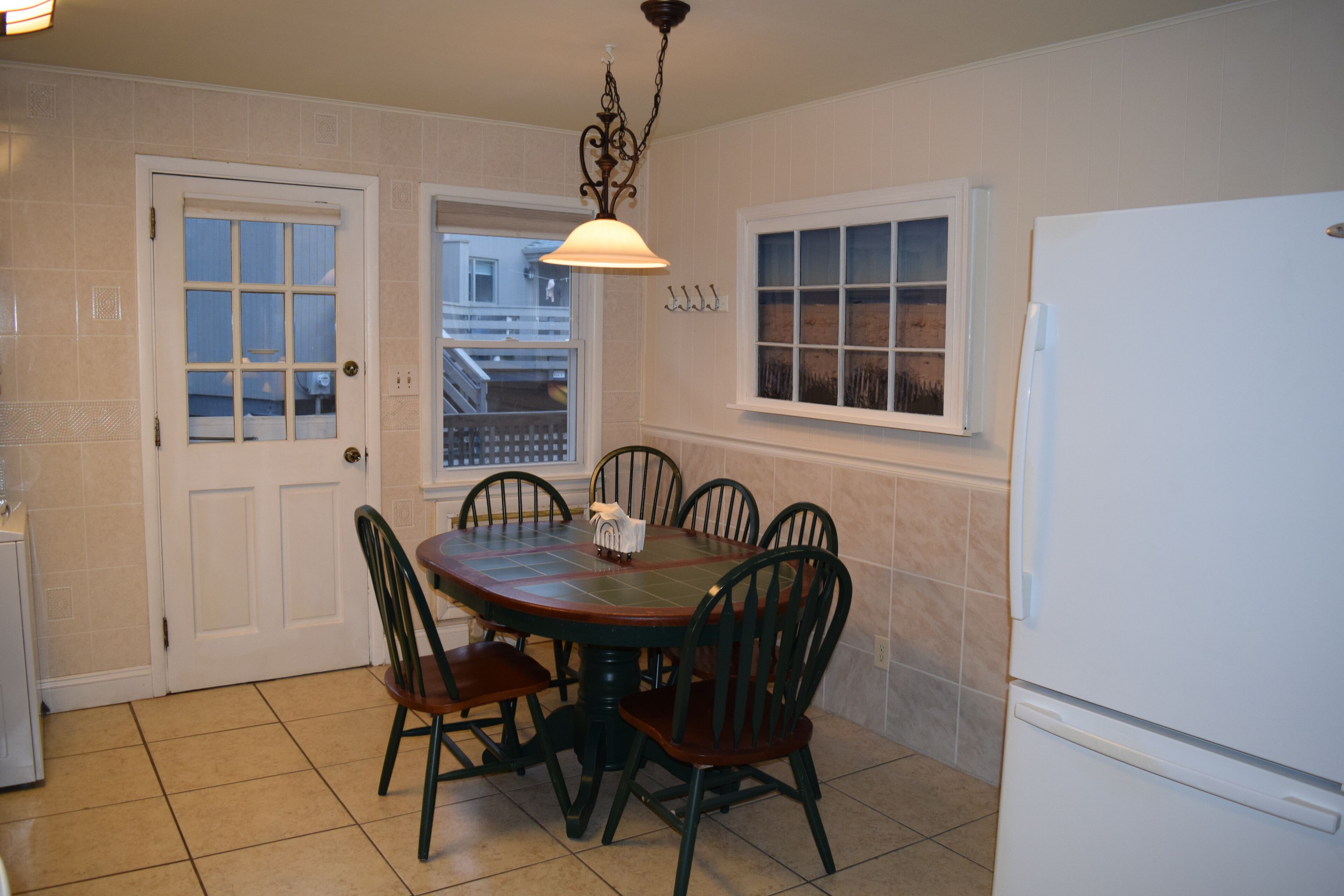 Una cocina con una mesa de comedor, sillas, un refrigerador y una ventana con vista a un balcón.