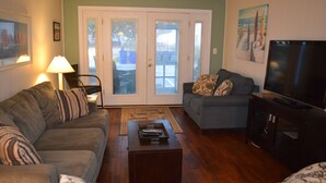 A living room with a sofa, a coffee table, a TV, and a door leading outside. - Pet Friendly Ocean Front Building Downtown Dewey Beach Sleeps 7 (Dewey Beach)