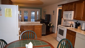 A kitchen with wooden cabinets, a white refrigerator, a microwave, an oven, and a dining table with chairs. - Pet Friendly Ocean Front Building Downtown Dewey Beach Sleeps 7 (Dewey Beach)