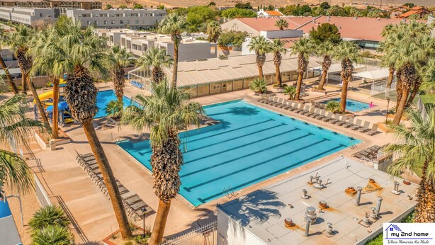 Un área de piscina con varias pistas de natación, palmeras y vistas de edificios y montañas circundantes.