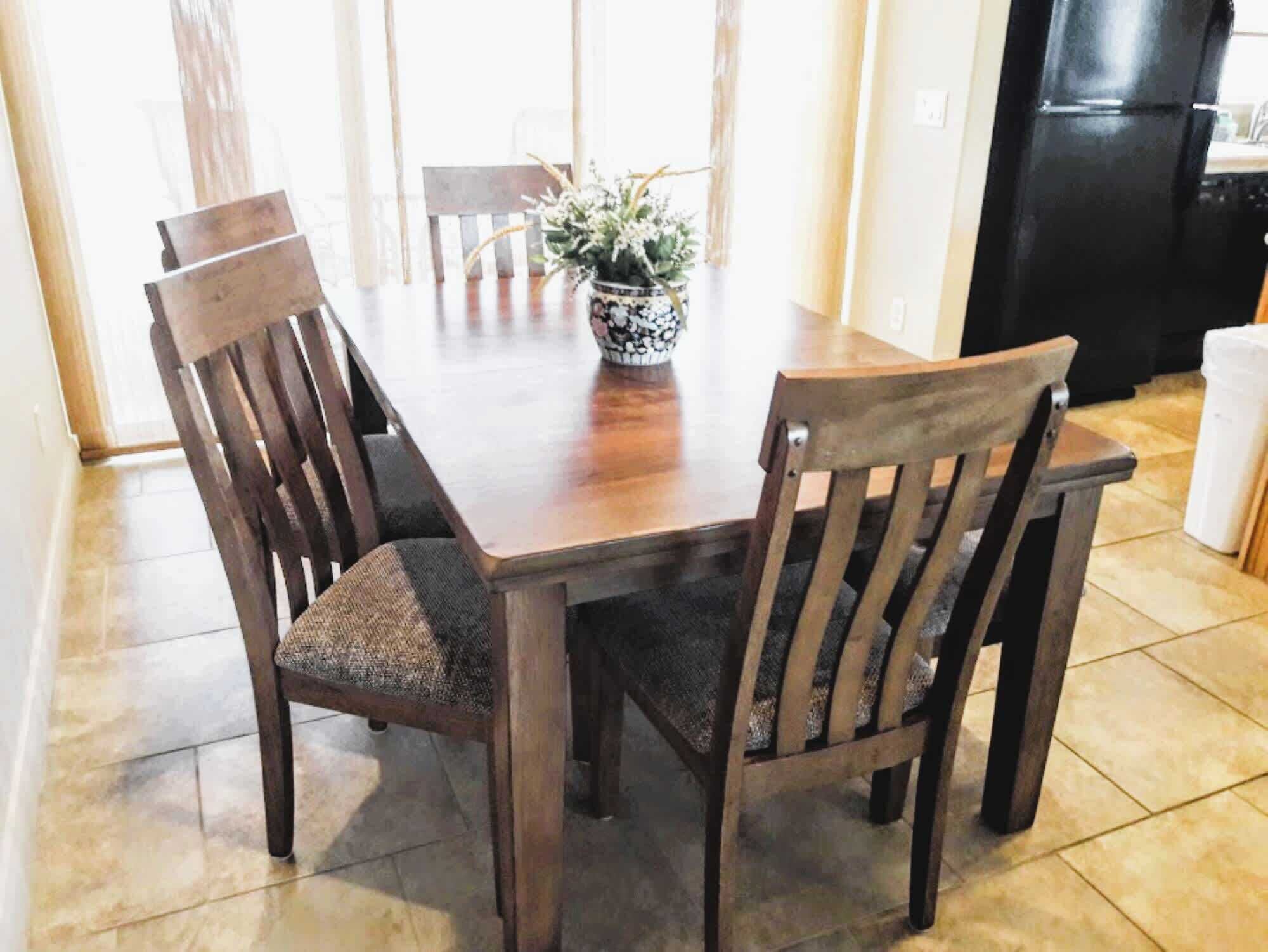 A dining table with four wooden chairs, a potted plant, and a black refrigerator in the background.