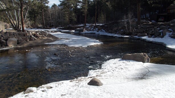 Une rivière dont les berges et les rochers sont couverts de neige, entourée d’arbres.