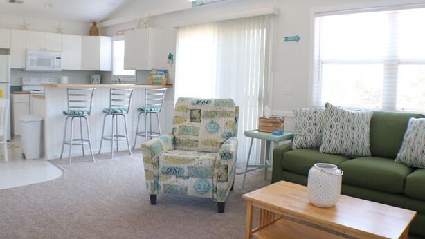 A compact living space with a kitchenette, a green sofa, a patterned armchair, and a small table.