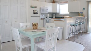 A compact kitchen with white cabinets, a microwave, a stove, and a small bar area with stools.