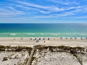 A beach with a wooden boardwalk leading to the shore, sandy beach, and clear blue sky.
