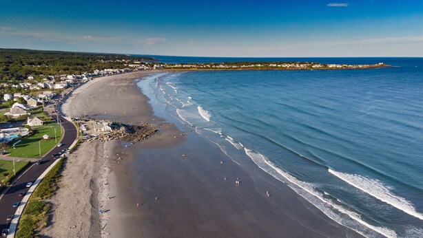 An aerial view of a coastal town with a beach, houses, and a road.