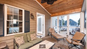 A covered porch with a green sofa, two chairs, and a table.