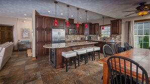 A kitchen with dark wood cabinets, a granite countertop, a stainless steel refrigerator, a microwave, a coffee maker, and a dining area with a wooden table and chairs.