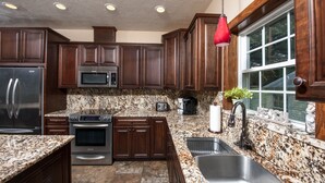 A kitchen with dark wooden cabinets, stainless steel appliances, granite countertops, and a window with a view.